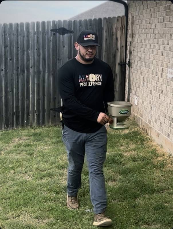 Technician carrying a Scotts spreader for lawn treatment